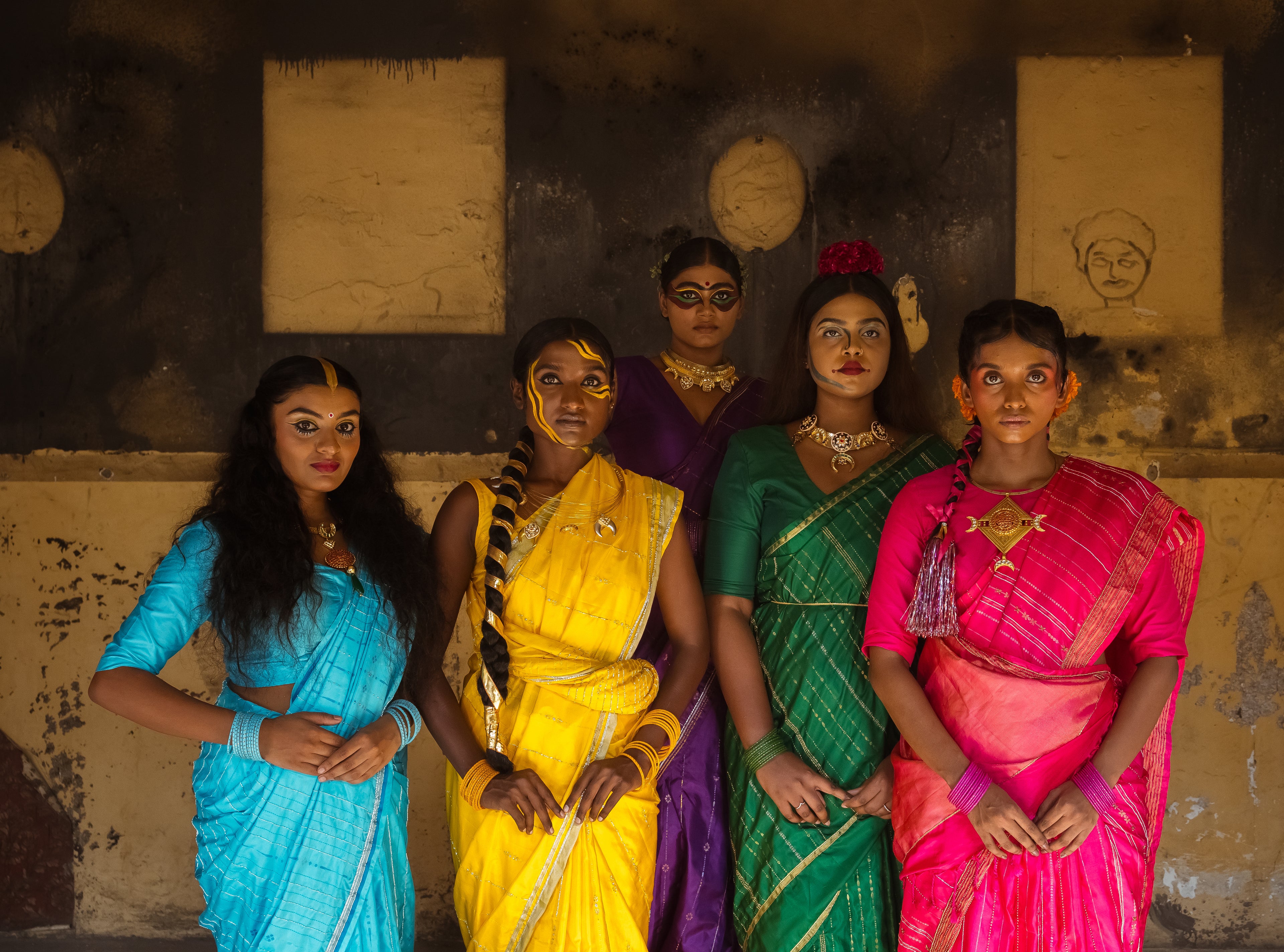 Five women standing next to each other with bright colourful (Blue,Yellow,Purple,Green & Pink) embroidered silk sarees.